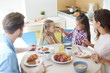 © pressmaster - One of girls taking her sister ponytail during breakfast by served table with their parents