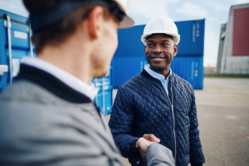 Smiling engineers standing in a freight yard shaking hands toget