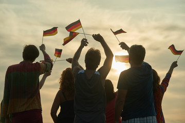 Wall Mural - Group of people waving deutch flags. German family against evening sky background.