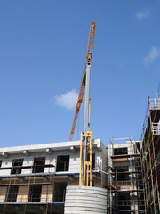 Wall Mural - A yellow construction crane working on a modern concrete apartment development with scaffolding with blue sky and sunlight