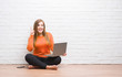 © Krakenimages.com - Young adult woman sitting on the floor over white brick wall using computer laptop surprised with an idea or question pointing finger with happy face, number one