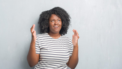 Canvas Print - Young african american plus size woman over grey grunge wall crazy and mad shouting and yelling with aggressive expression and arms raised. Frustration concept.