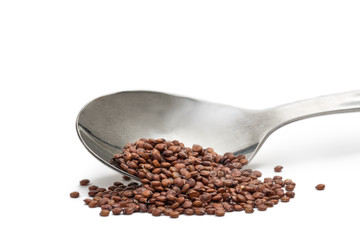 Wall Mural - Close up of tilted metal spoon with red quinoa seeds isolated on white background