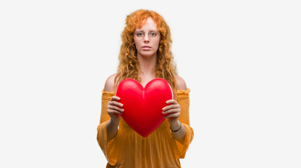 Poster - Young redhead woman in love holding red heart with a confident expression on smart face thinking serious