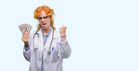 Sticker - Young redhead doctor woman holding dollars annoyed and frustrated shouting with anger, crazy and yelling with raised hand, anger concept