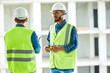 © Seventyfour - Serious confident middle-eastern worker in glasses and hardhat attentively listening to colleagues while they standing at apartment block site