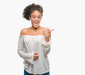 Young afro american woman wearing glasses over isolated background smiling with happy face looking and pointing to the side with thumb up.