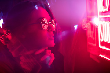 Long hair girl with sunglasses and leather jacket looking at neon lights