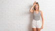 © Krakenimages.com - Young beautiful blonde woman over white brick wall surprised with hand on head for mistake, remember error. Forgot, bad memory concept.