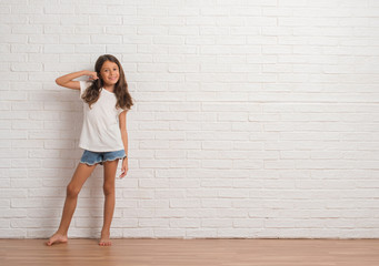 Wall Mural - Young hispanic kid stading over white brick wall smiling doing phone gesture with hand and fingers like talking on the telephone. Communicating concepts.