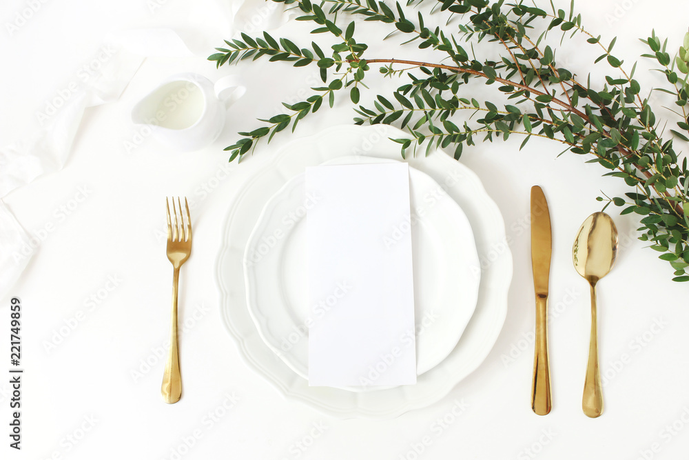 Festive wedding, birthday table setting with golden cutlery, eucalyptus parvifolia branch, porcelain plate, milk and silk ribbon. Blank card mockup. Rustic restaurant menu concept. Flat lay, top view - obrazy, fototapety, plakaty 