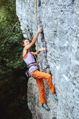 Wall Mural - young slim female rock climber climbing on the cliff