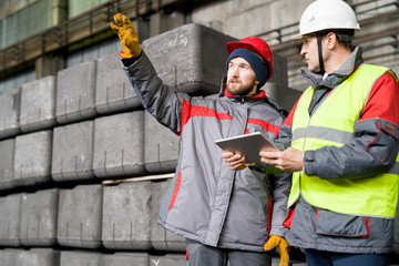 Waist up portrait of modern bearded worker  wearing warm jacket and hardhat pointing up while discussing production with foreman  in workshop, copy space