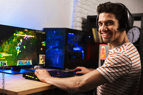 Fotomural Image of cheerful gamer man playing video games on computer, wearing headphones