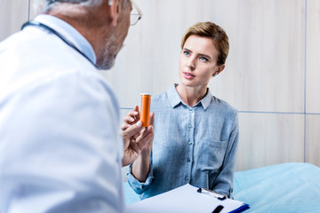 partial view of male doctor with clipboard giving pills to female patient in hospital room