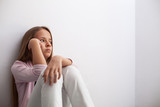 Pensive young teenager girl sitting by the wall on the floor