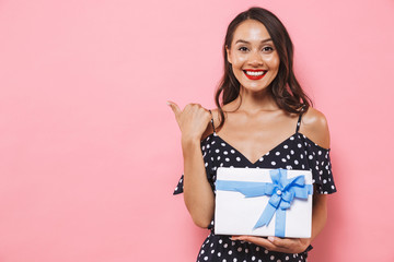 Happy woman isolated over pink background holding susprise gift box pointing.