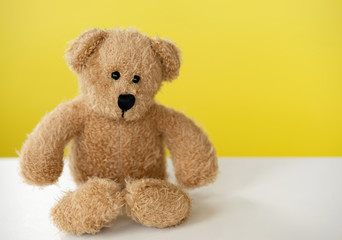 Wall Mural - Portrait of teddy bear sitting alone on white table with yellow background, One brown bear toy with with copy space