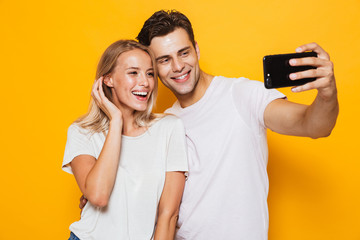 Canvas Print - Young loving couple standing isolated over yellow wall background take a selfie by mobile phone.