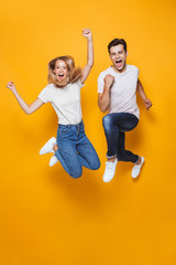 Wall Mural - Young loving couple jumping isolated over yellow wall background.