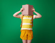 pupil with backpack on green background hiding behind book