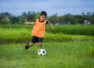 8 or 9 years old happy and excited kid playing football outdoors in garden wearing training vest running and kicking soccer ball