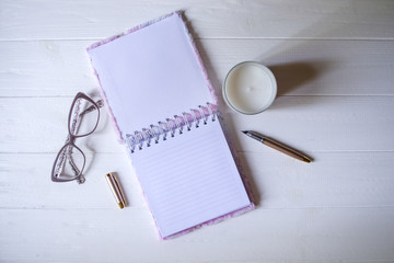 Wall Mural - The opened notepad, pen, white candle, glasses and branches of hops as decoration on a white wooden table. Desktop still life with space for text.