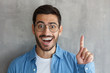 © Damir Khabirov - Closeup picture of young handsome European Caucasian male isolated on grey background wearing denim T-shirt and eyeglasses pointing upwards with excited face as if having seen beneficial offer