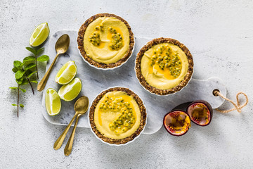 vegan raw mini tarts from nuts and dates with cashew cream from mango purée with lime juice and seeds of passion fruit. healthy alternative food on a white marble board