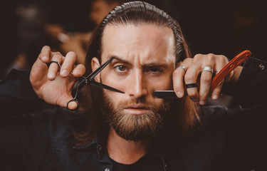 Wall Mural - Portrait of man with beard hairdresser. Barber is holding razor and scissors in his hands barbershop.