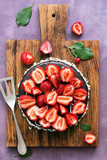 Fototapeta Zwierzęta - Chocolate cake decorated with fresh strawberries on a cutting board, purple background. Top view,flat lay