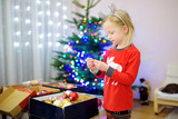 Fototapeta Na ścianę - Adorable little girl decorating the Christmas tree with colorful glass baubles. Trimming the Christmas tree.