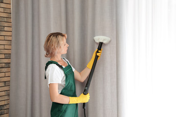 Poster - Female janitor removing dust from curtain with steam cleaner indoors