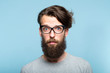 worried nervous alarmed bearded hipster guy wearing cat eye glasses. stylish modern fashionist. portrait of a geeky quirky eccentric man on blue background.