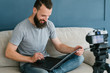 © golubovy - content creation for social media. bearded man holding laptop and shooting video of himself using camera on tripod. modern technology and blogging freelance work concept.