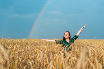 Wall Mural - Young smiling girl in a field with Golden wheat and rainbow with hands in hand.