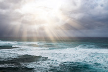 Rays Of Sunlight Break Through Storm Clouds Above The Open Ocean Waves In A Heavenly Seascape