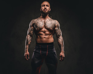 Bearded shirtless tattooed athlete in sportswear. Isolated on a dark textured background.