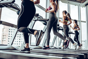 side view of young beautiful women looking away while running on treadmill at gym
