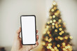 © sonyachny - christmas mockup with space for text. christmas advertising, app template. hand holding phone with empty screen on background of golden beautiful christmas tree with lights
