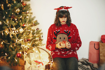 Wall Mural - happy girl in reindeer antlers holding gift box at golden beautiful christmas tree with lights in festive room. winter holiday atmospheric moments. seasons greetings. Merry Christmas