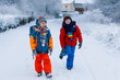 © Irina Schmidt - Two little kids boys of elementary class walking to school during snowfall. Happy children having fun and playing with first snow. Siblings ans friends with backpack in colorful winter clothes.