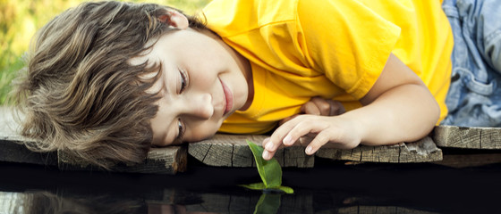 Wall Mural - boy play with autumn leaf ship in water, children in park play with leaf in river