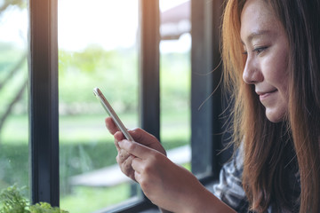 Canvas Print - Closeup image of an asian woman holding , using and looking at smart phone with blur green nature background