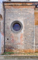 Wall of ancient Orthodox Christian church with round window and colored glass. Built between the 14th and 17th centuries. Style: gothic exterior and baroque interior. Brescia, Italy.