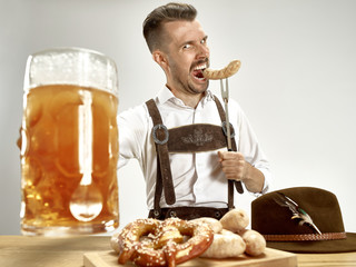 Germany, Bavaria, Upper Bavaria. The young happy smiling man with beer dressed in traditional Austrian or Bavarian costume holding mug of beer at pub or studio. The celebration, oktoberfest, festival