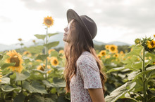 Young Brunette Girl With A Hat And Glasses Posing And Walking In The Middle Of A Countryside Of Sunflowers