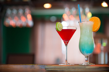 Cosmopolitan and Blue Hawaiian cocktails on the bar counter, blue and red drinks decorated with orange and lime in the pub