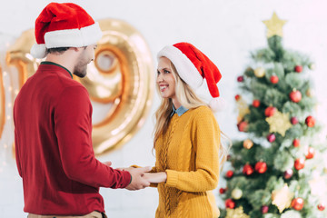 Sticker - happy couple in santa hats holding hands and looking at each other on christmas eve