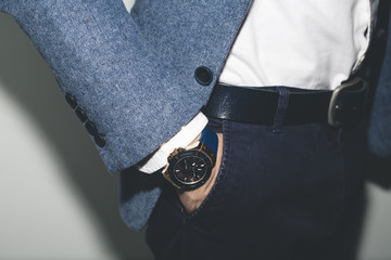 Wall Mural - Closeup fashion image of luxury watch on wrist of man.body detail of a business man.Man's hand in blue pants pocket closeup at white background.Man wearing blue jacket and white shirt.Not isolated